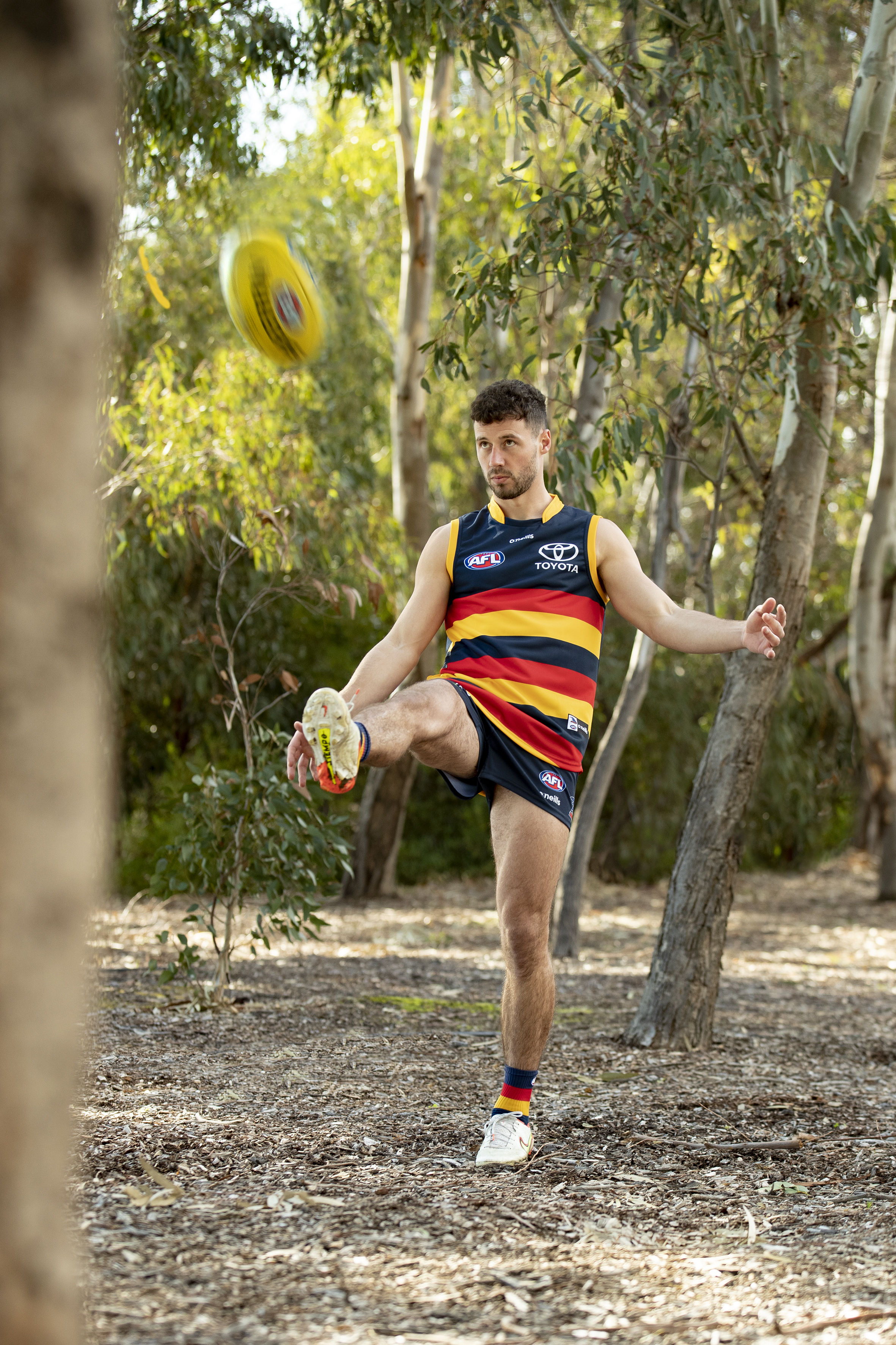 Luke Brown kicking a football in a forest.