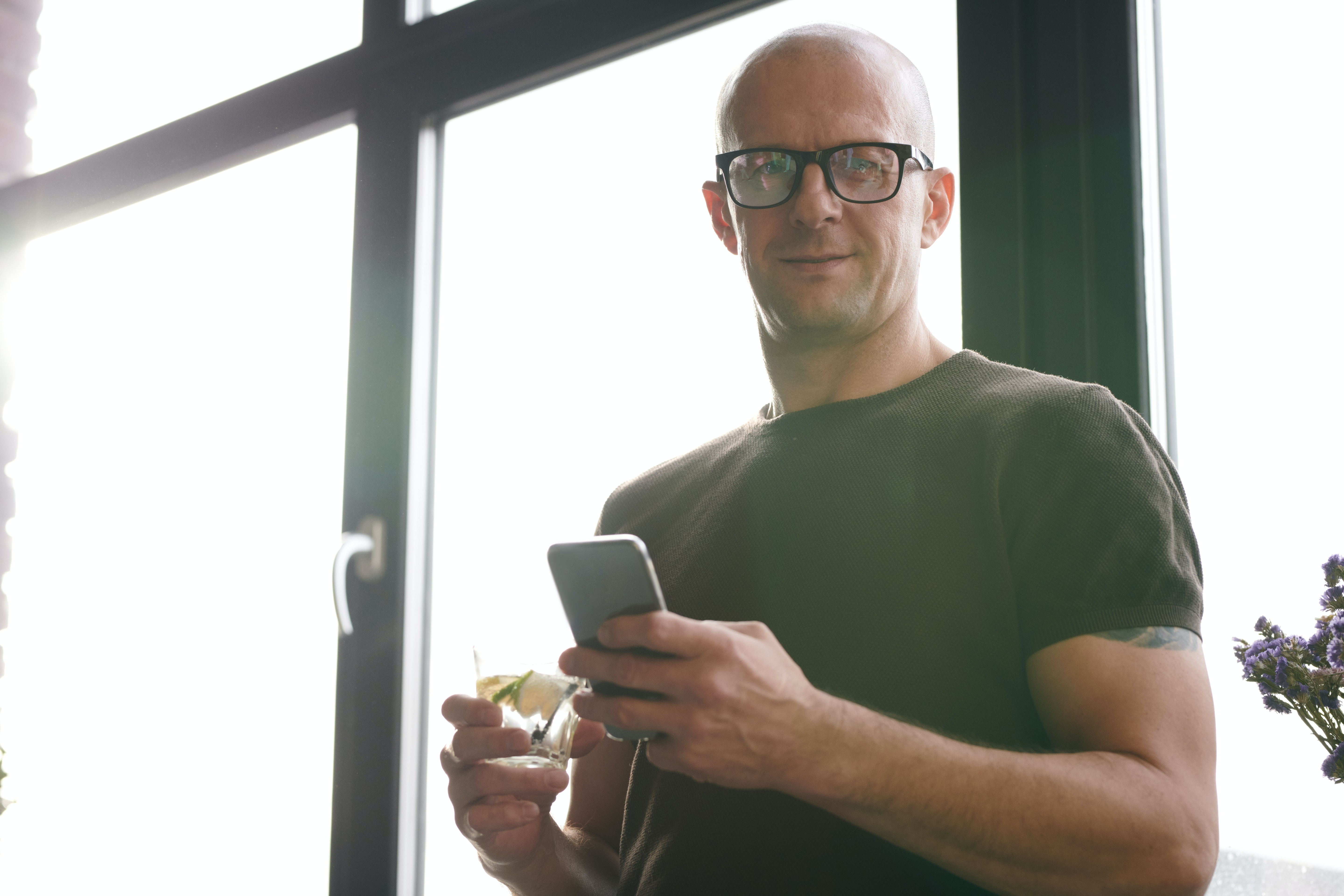 Bald guy wearing glasses and holding his phone showing off his look with glasses