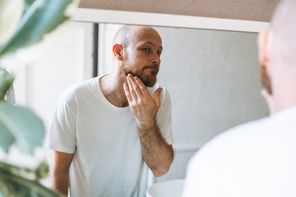 A bald man with healthy skin looking at a mirror checking his face