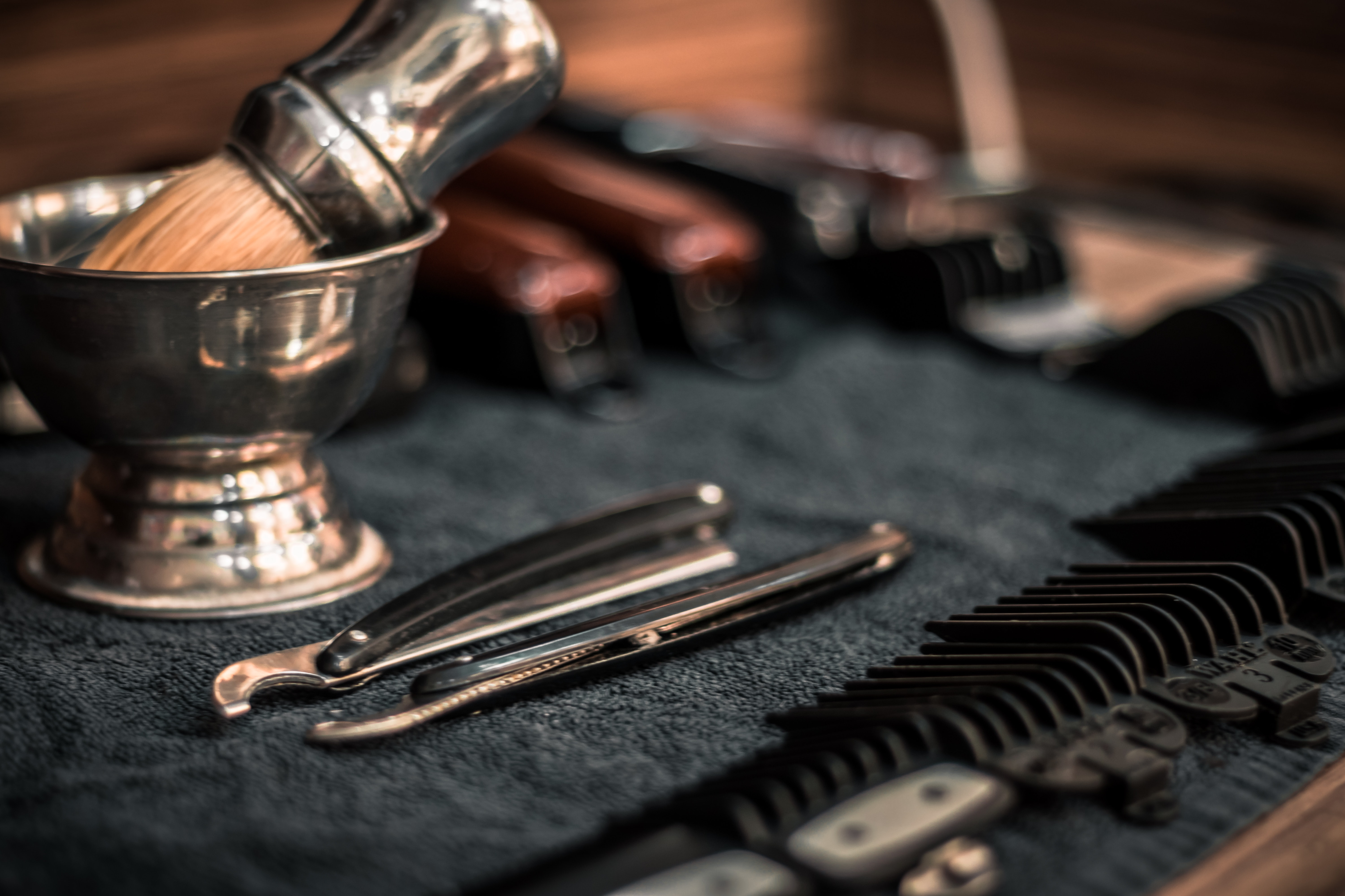 multiple electric shavers and attachments lined up on a barber's table with straight razors 