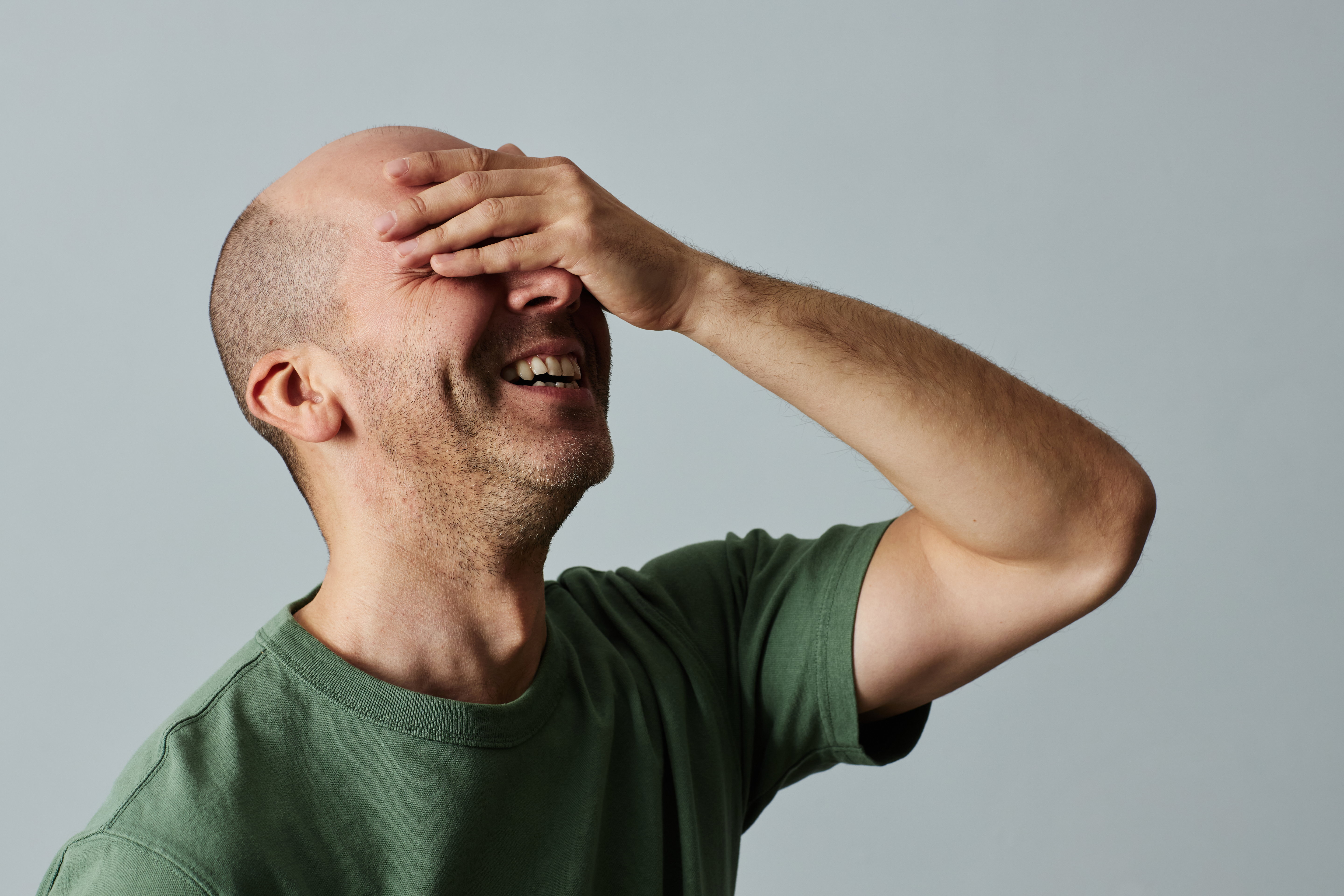 bald man laughing with hand coveering face