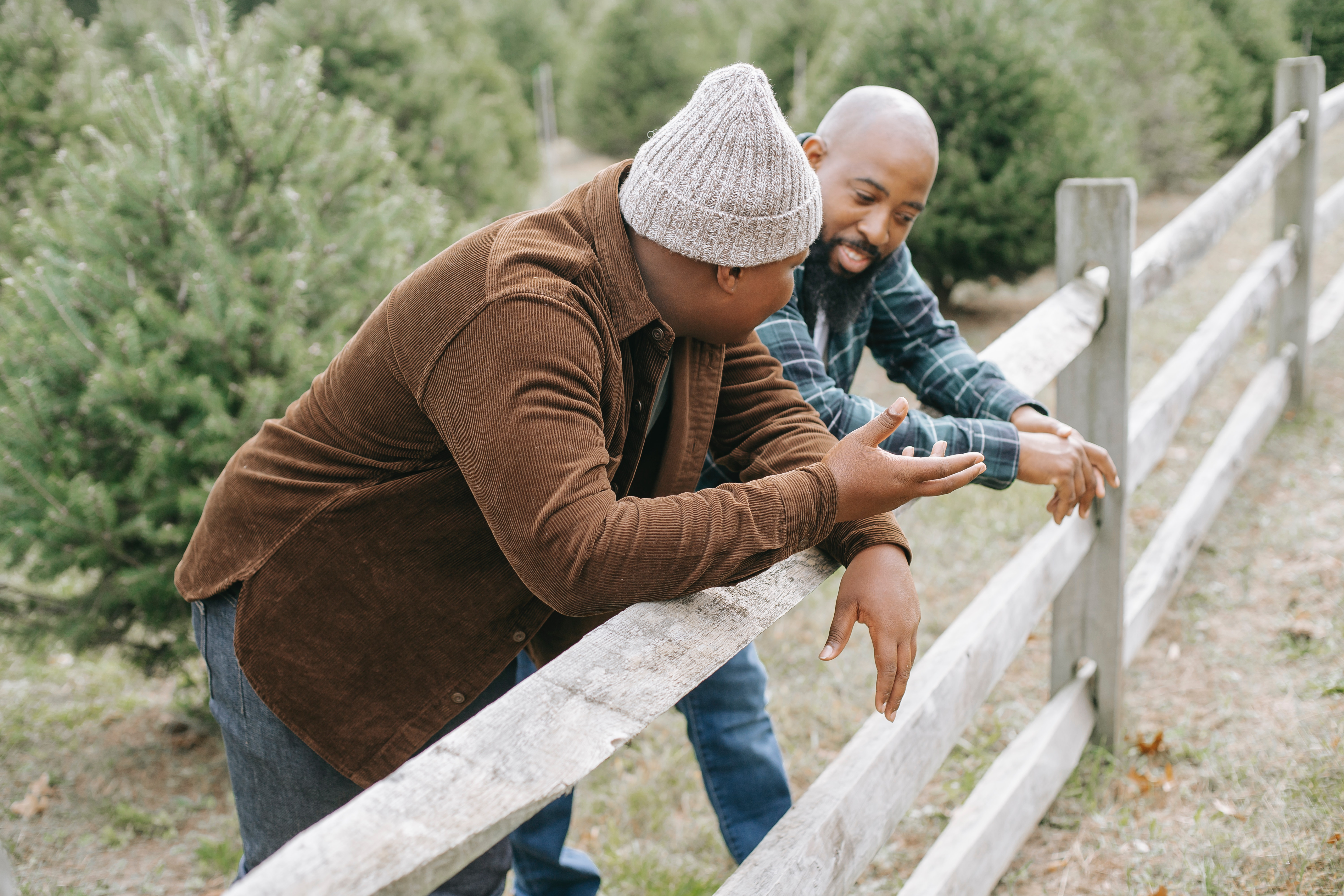 bald guy talking with another bald guy wearing a bonnet with both leaning over a fence