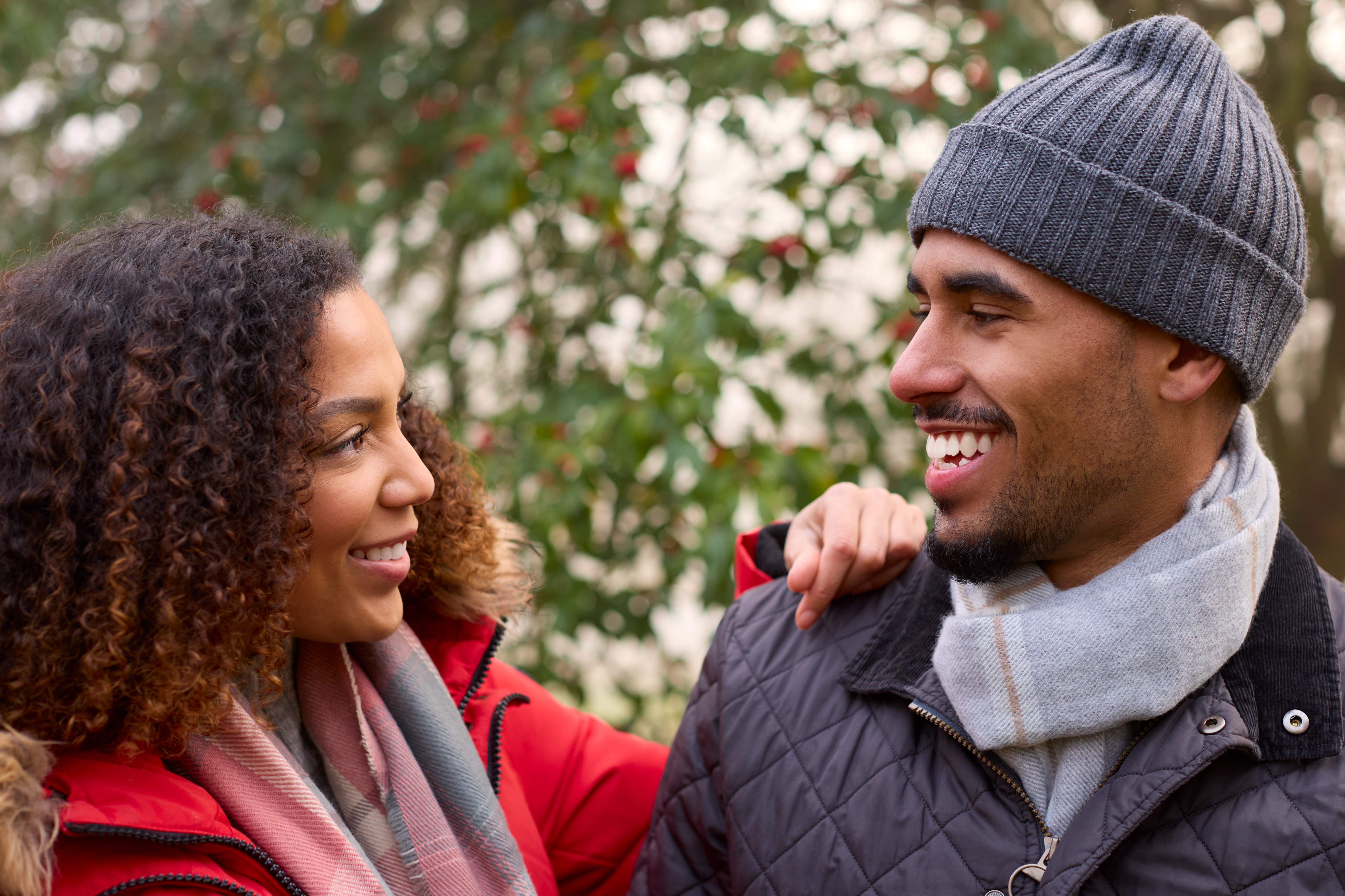 bald man smiling wearing a beanie and looking at his girlfriend 