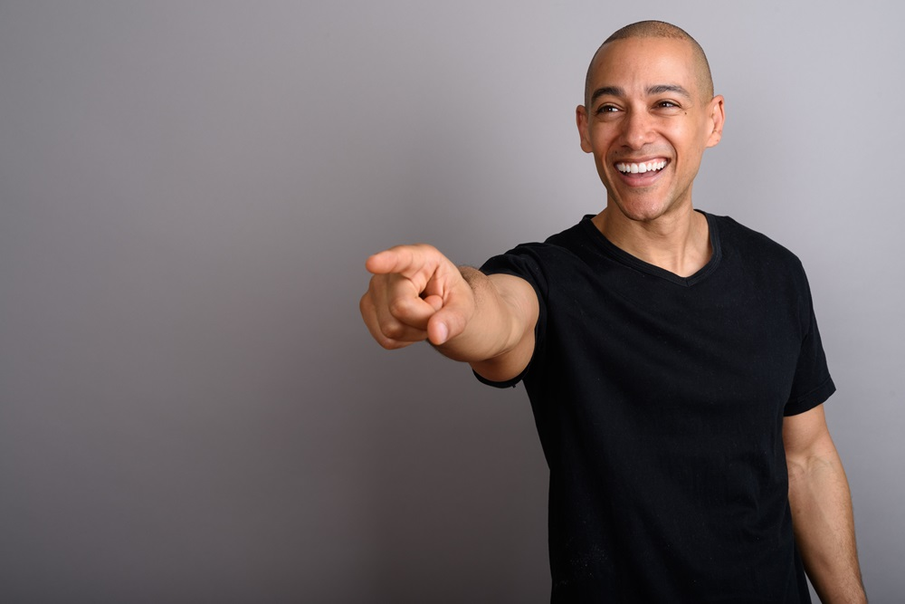 photo of bald man smiling and pointing towards someone