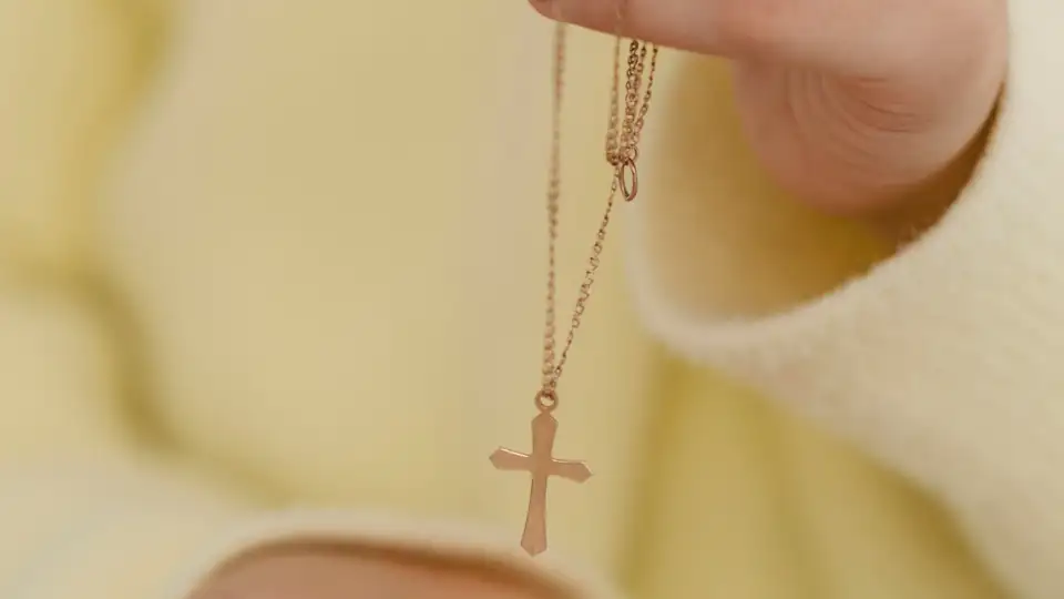 woman in yellow dress holding a rose gold cross necklace from Glor-e