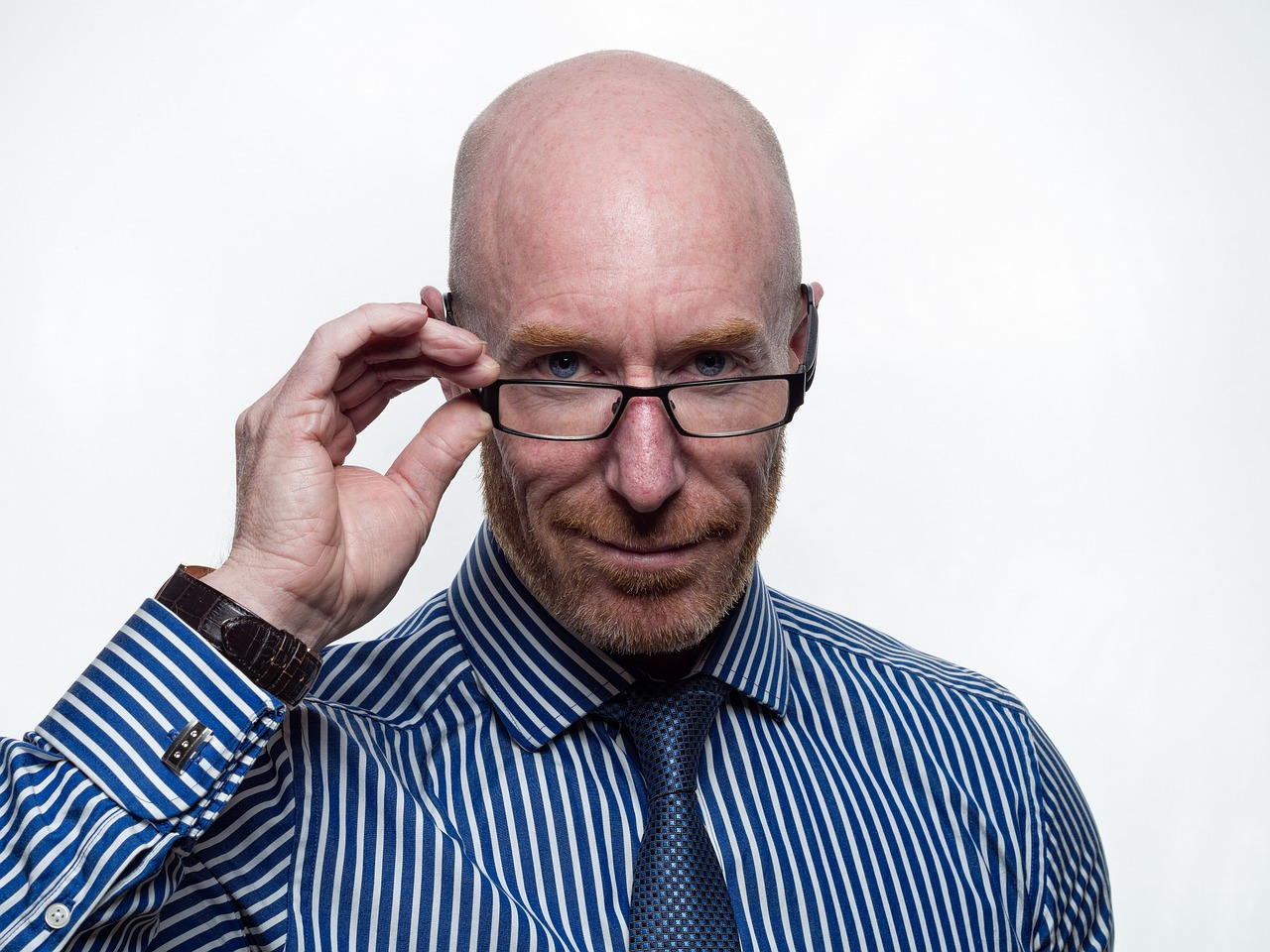 A bald male executive holding the frame of his glasses and looking straight with confidence