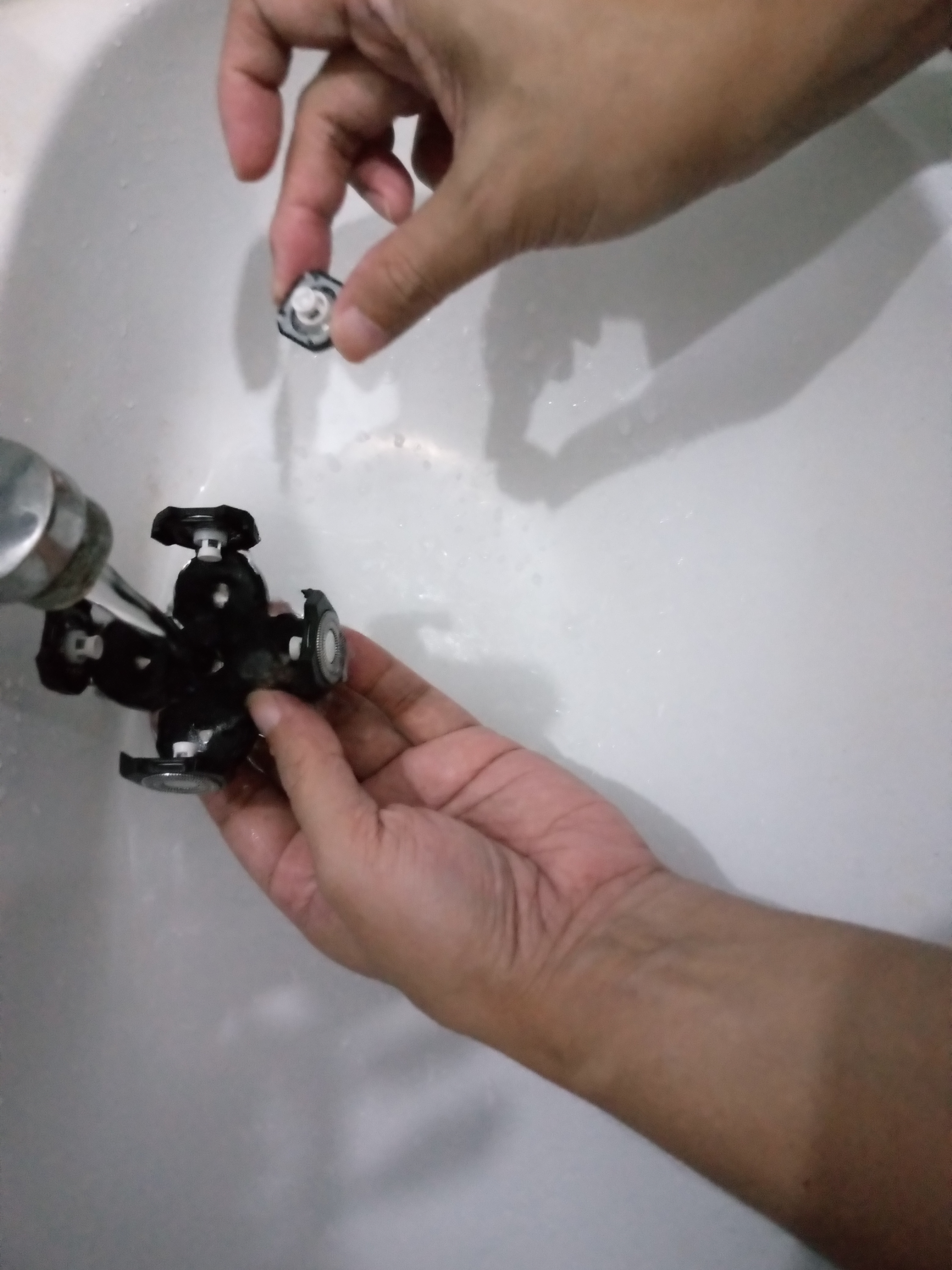 5 head rotary shaver blades being washed with water in a bathroom sink