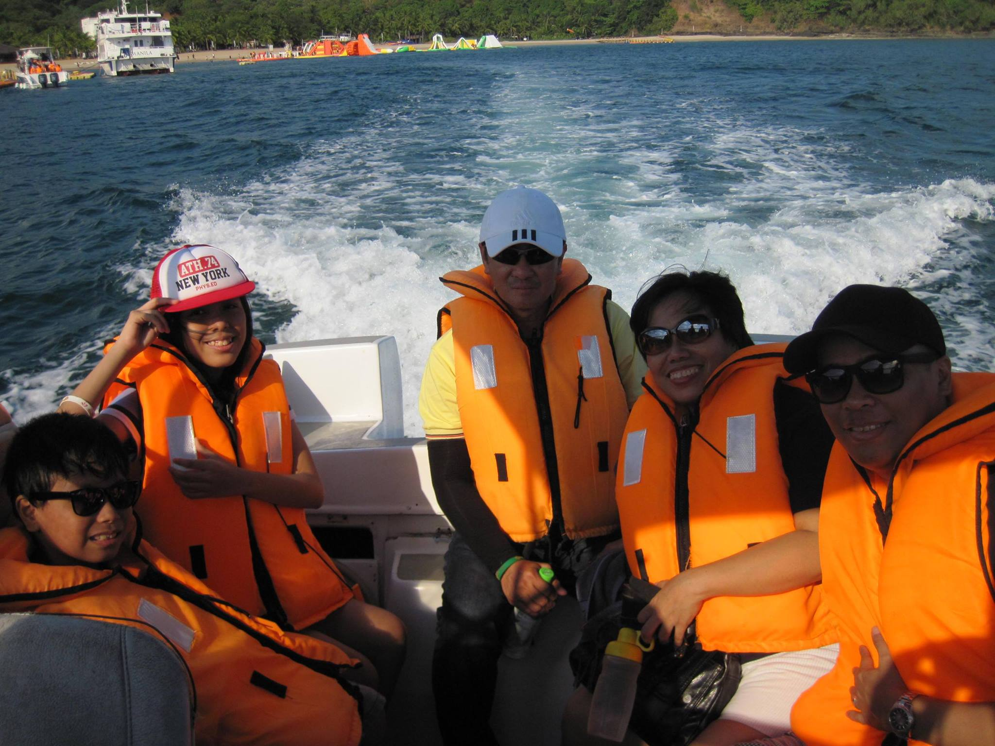 a bald guy wearing a baseball cap riding a speedboat with four companions