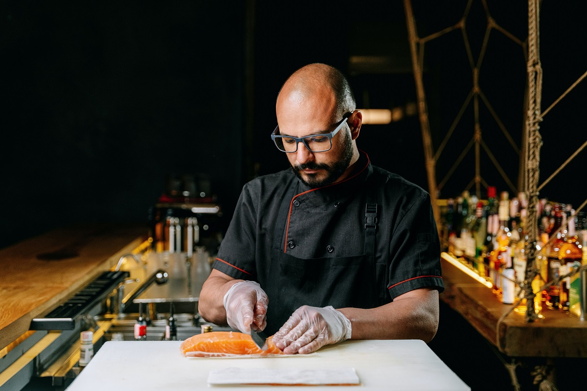 bald chef wearing glasses while cutting a salmon belly