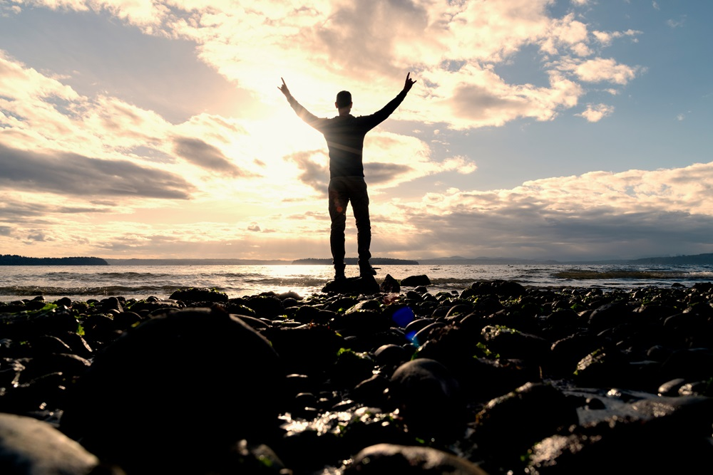 man with his arms raised facing an amazing sunset at the beach