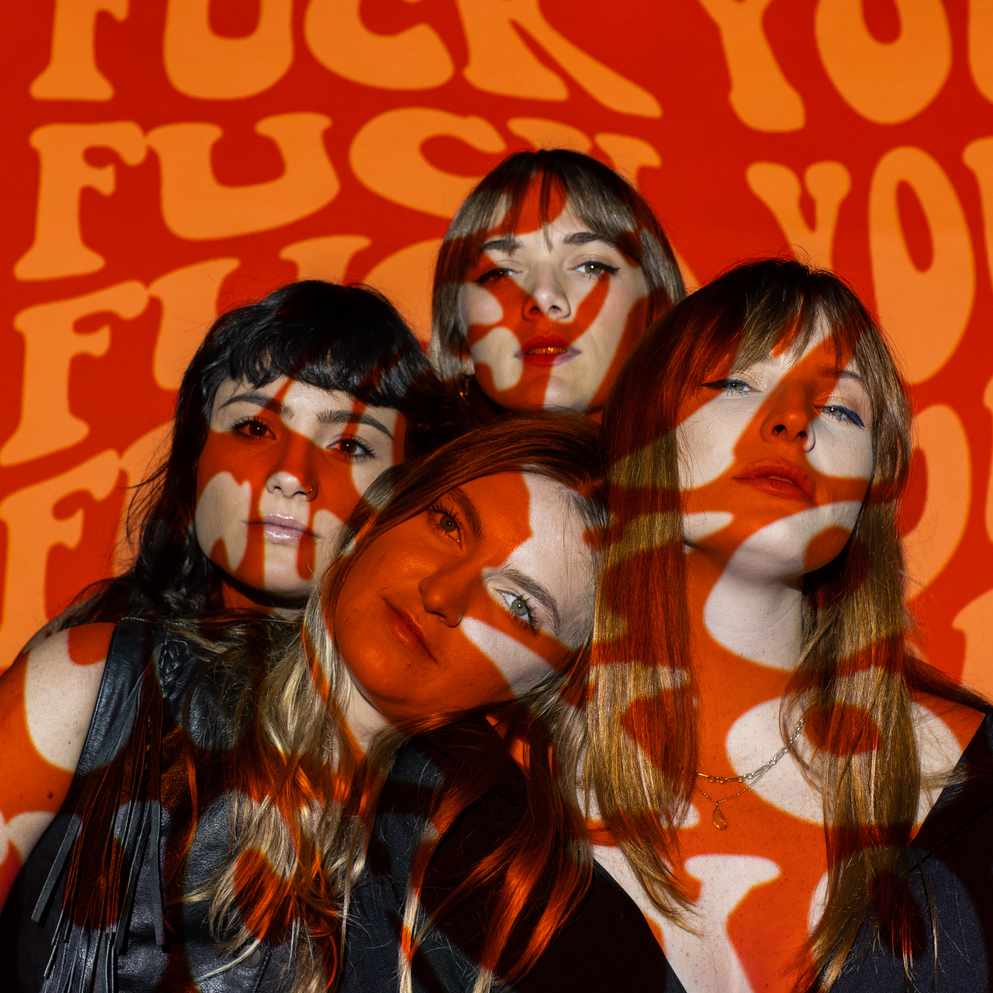 (From left to right) Betty Taylor's Katie Ishaque, Claire Chittick, Kayla Smart and Sophie Patrick posing in front of a projected orange background that says 'F*ck You' in a wavy font.