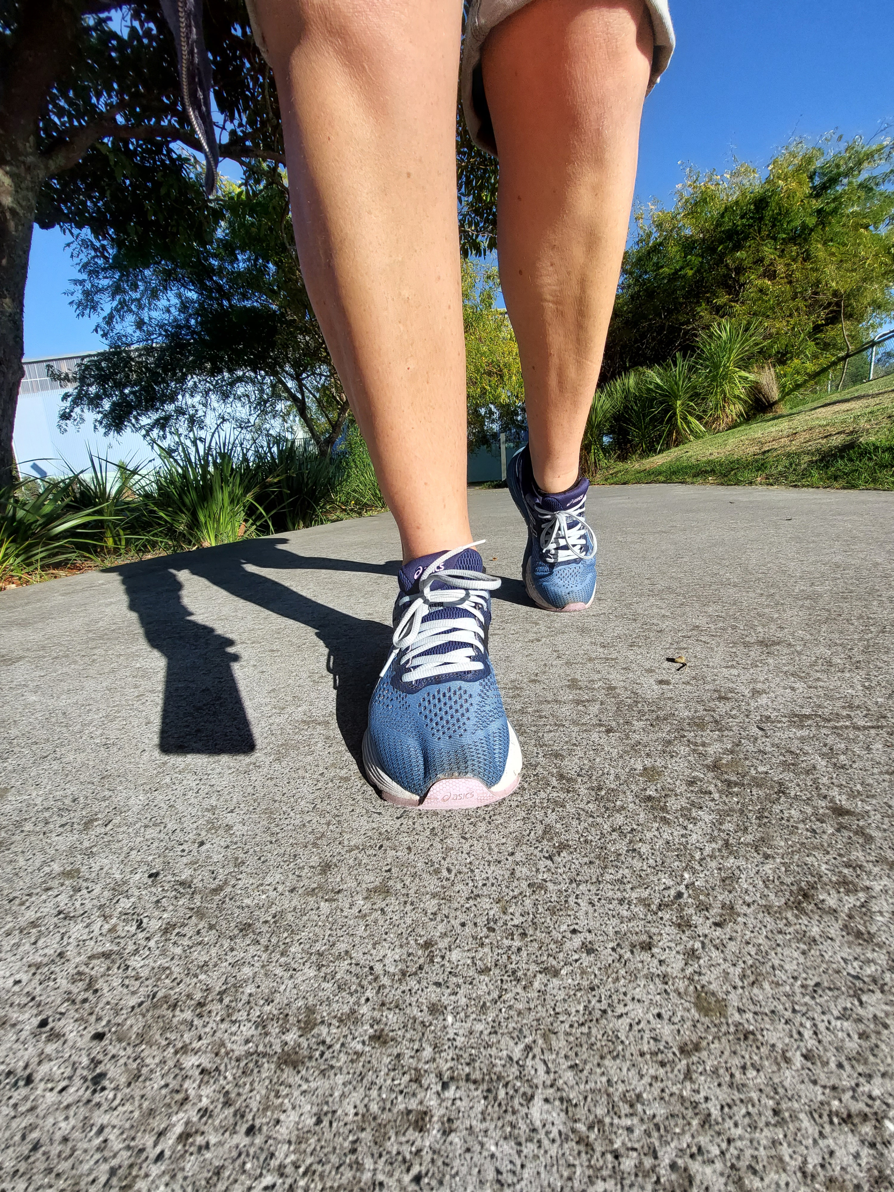 feet walking on a path showing the shadow of cellphone carried in hand