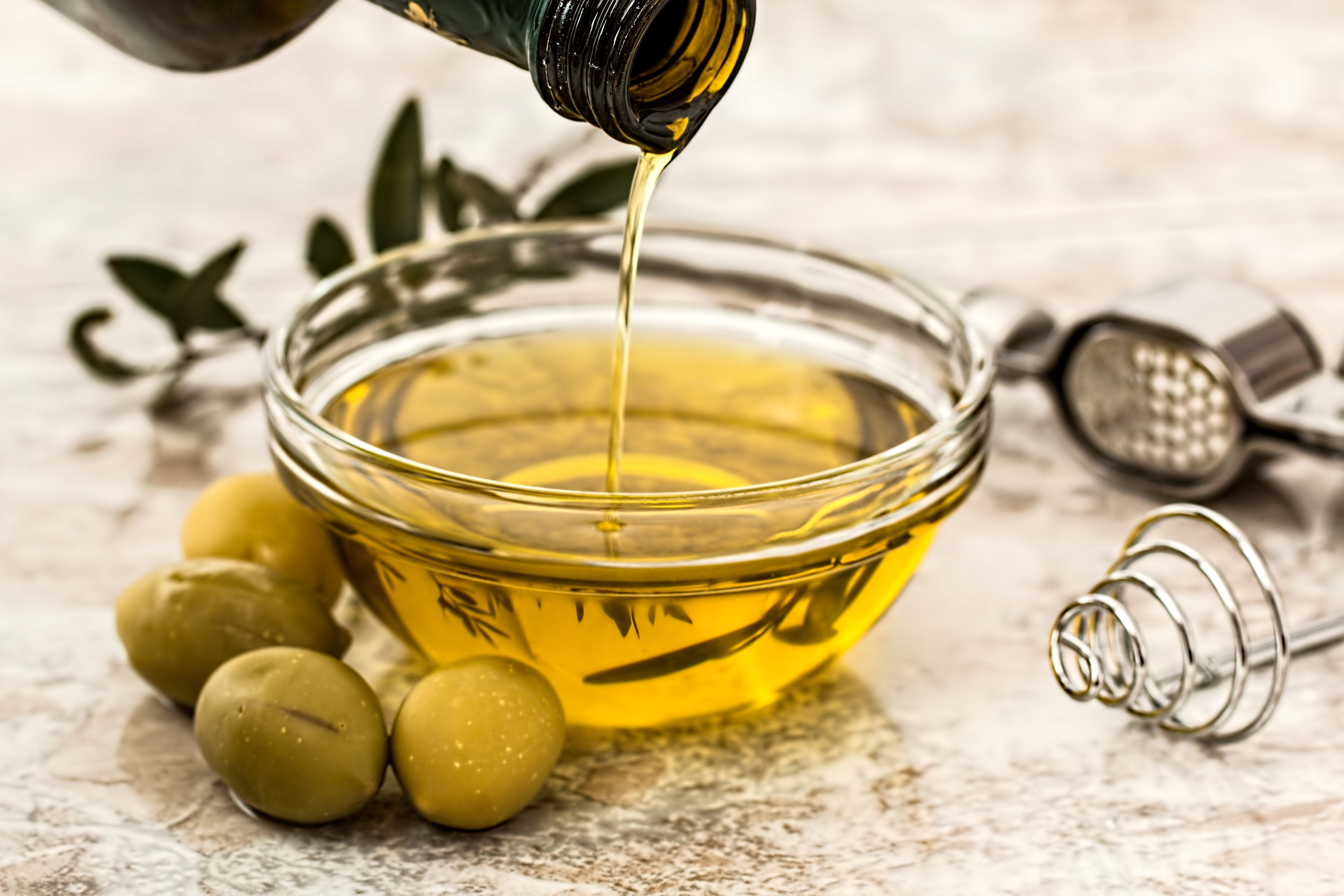 jojoba oil being poured in a dish with jojoba seeds beside it